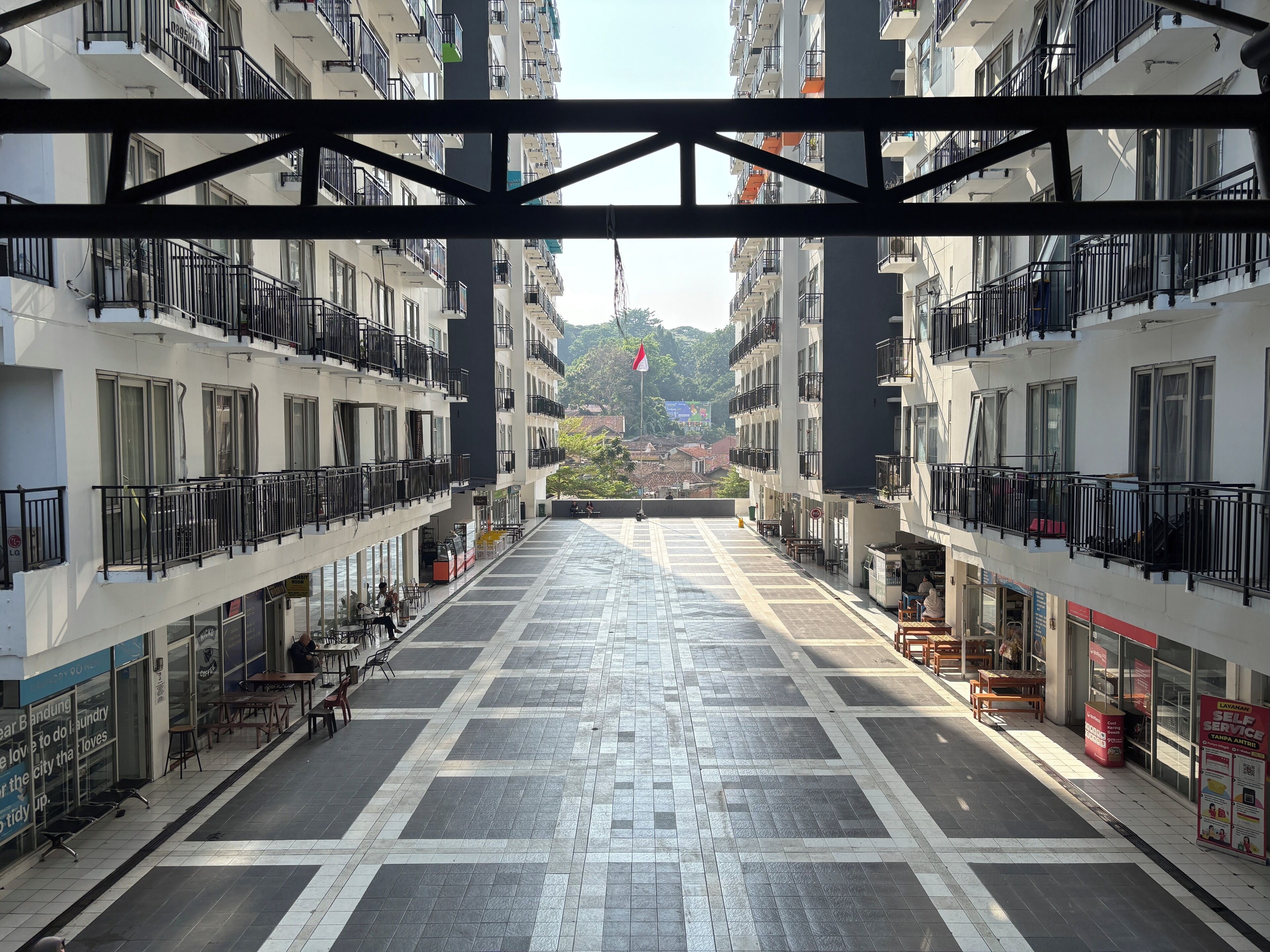 A multi-story building with balconies, a tiled plaza, and storefronts.