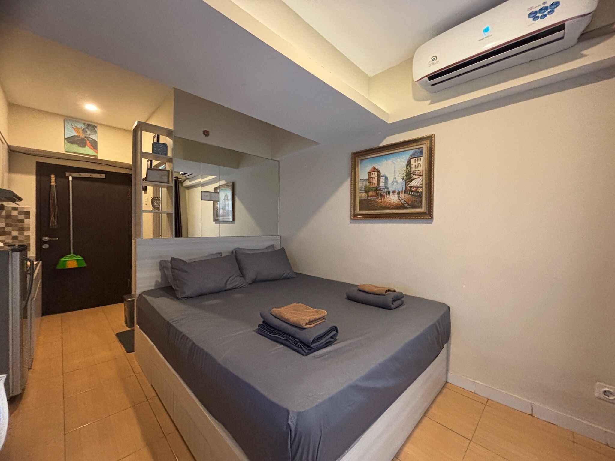 Une chambre à coucher avec un lit, un tableau, un climatiseur et une porte sur laquelle est accroché un balai.