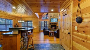 L’intérieur d’une cabane en rondins, avec une cheminée en pierre, des murs en bois, un sol en pierre et un coin bar.