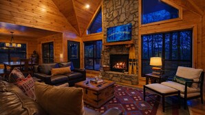 Un intérieur de chalet chaleureux avec une cheminée en pierre, des meubles en cuir et de grandes fenêtres.
