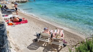 En strand med klart, blåt vand, folk der solbader, og en svane i det fjerne.