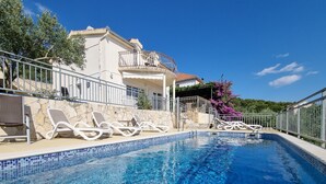En swimmingpool med liggestole, en stenvæg og en bygning med balkon.