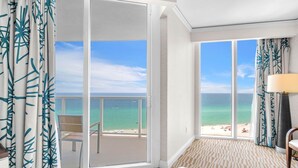 Een hotelkamer met een grote glazen schuifdeur die uitkomt op een balkon met uitzicht op het strand.