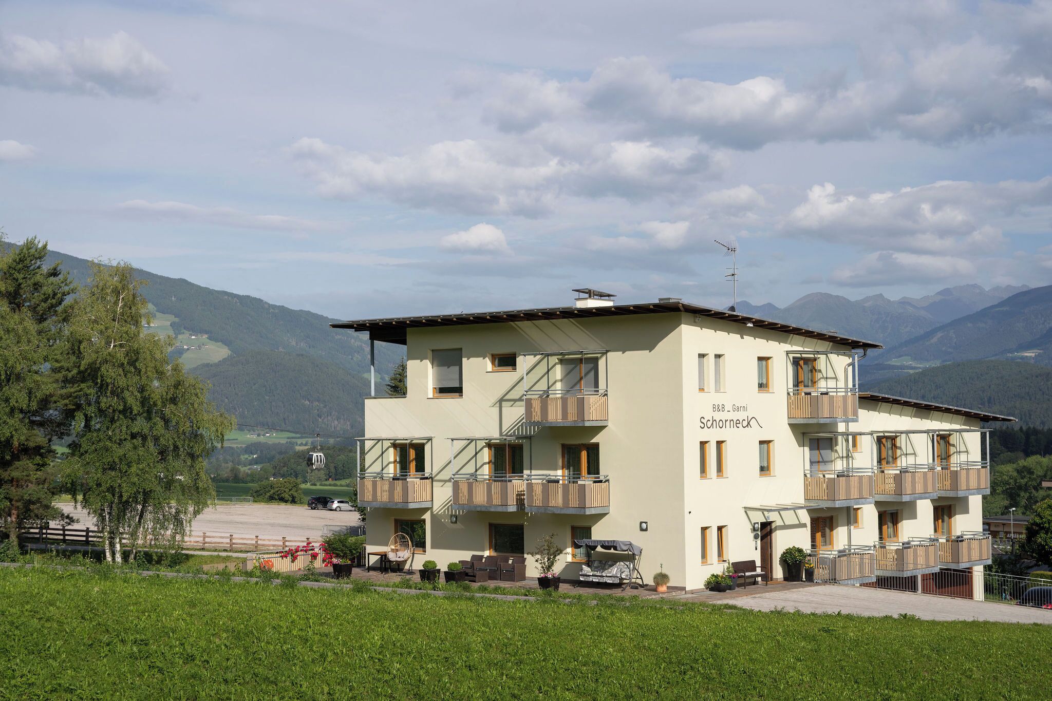 Ein mehrstöckiges Hotel mit Balkonen, einem Parkplatz und Blick auf Berge.