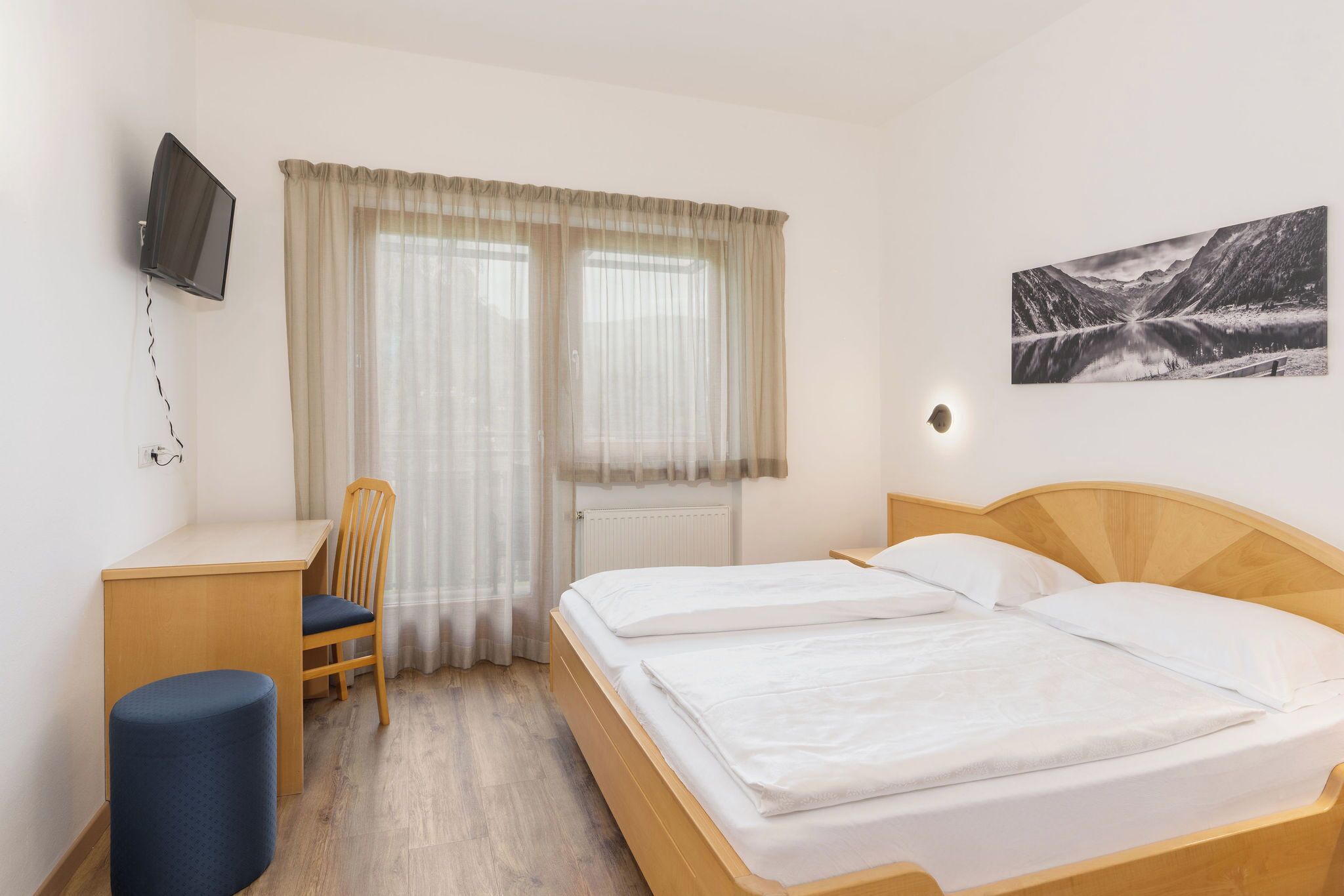 Ein Hotelzimmer mit Bett, Schreibtisch, Stuhl, Fernseher und einem Fenster mit Vorhängen.