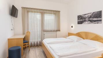 Ein Hotelzimmer mit Bett, Schreibtisch, Stuhl, Fernseher und einem Fenster mit Vorhängen.
