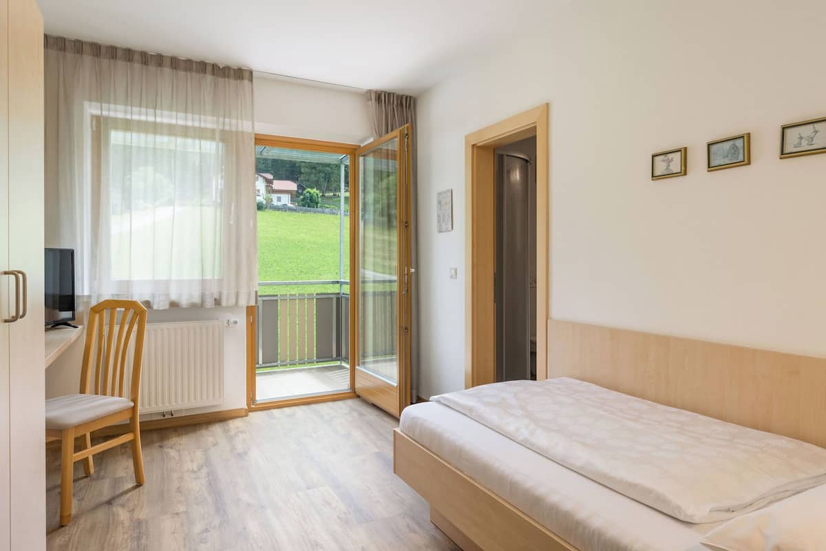 A bedroom with a bed, a chair, a desk, and a window with a view of a green landscape.