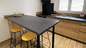 A kitchen with a dark countertop, wooden stools, a black range hood, and a window with blinds. - U Pianeddu (Olivese)