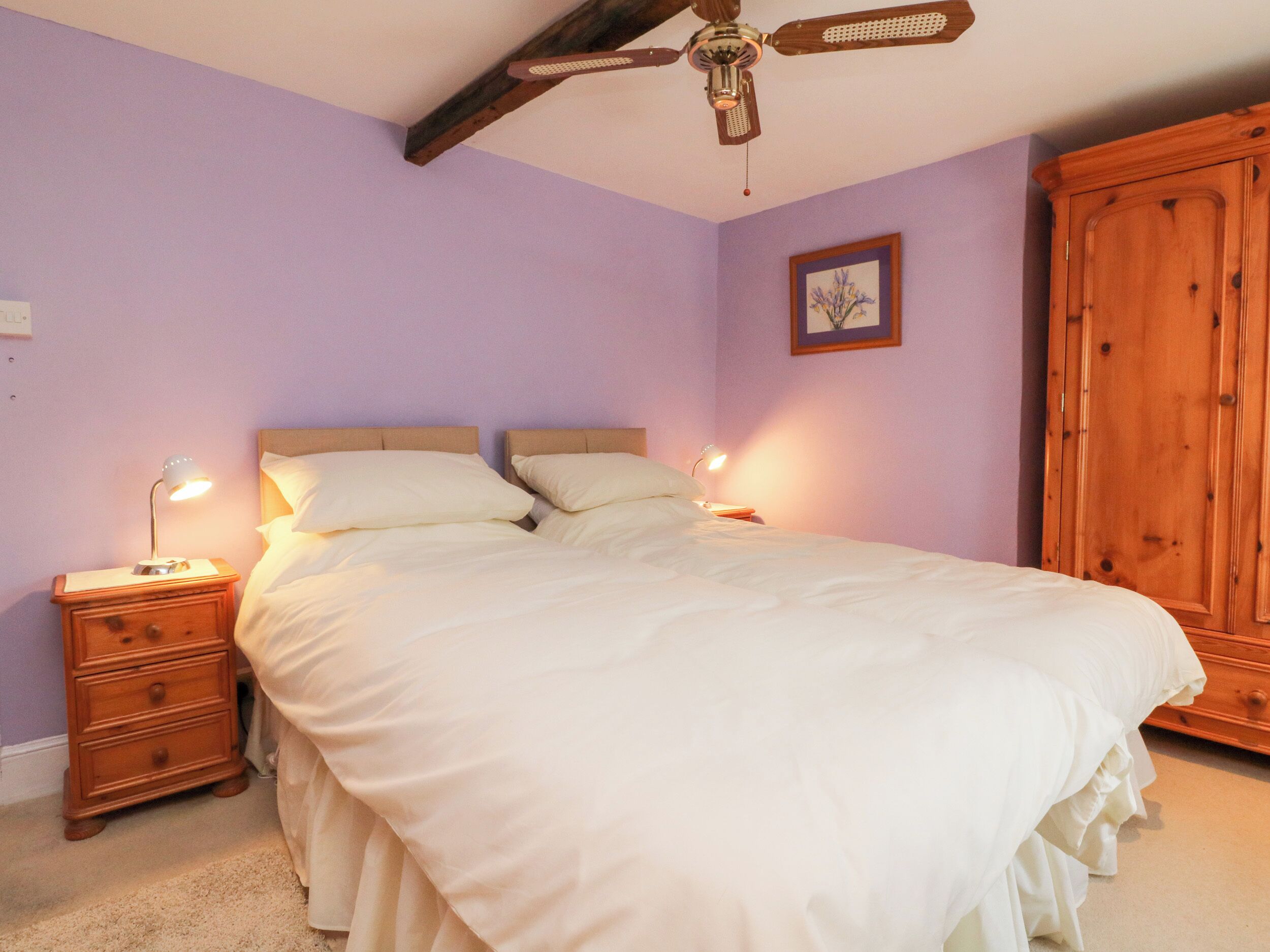 Une chambre à coucher avec un lit, des tables de chevet en bois, un ventilateur de plafond et une armoire.