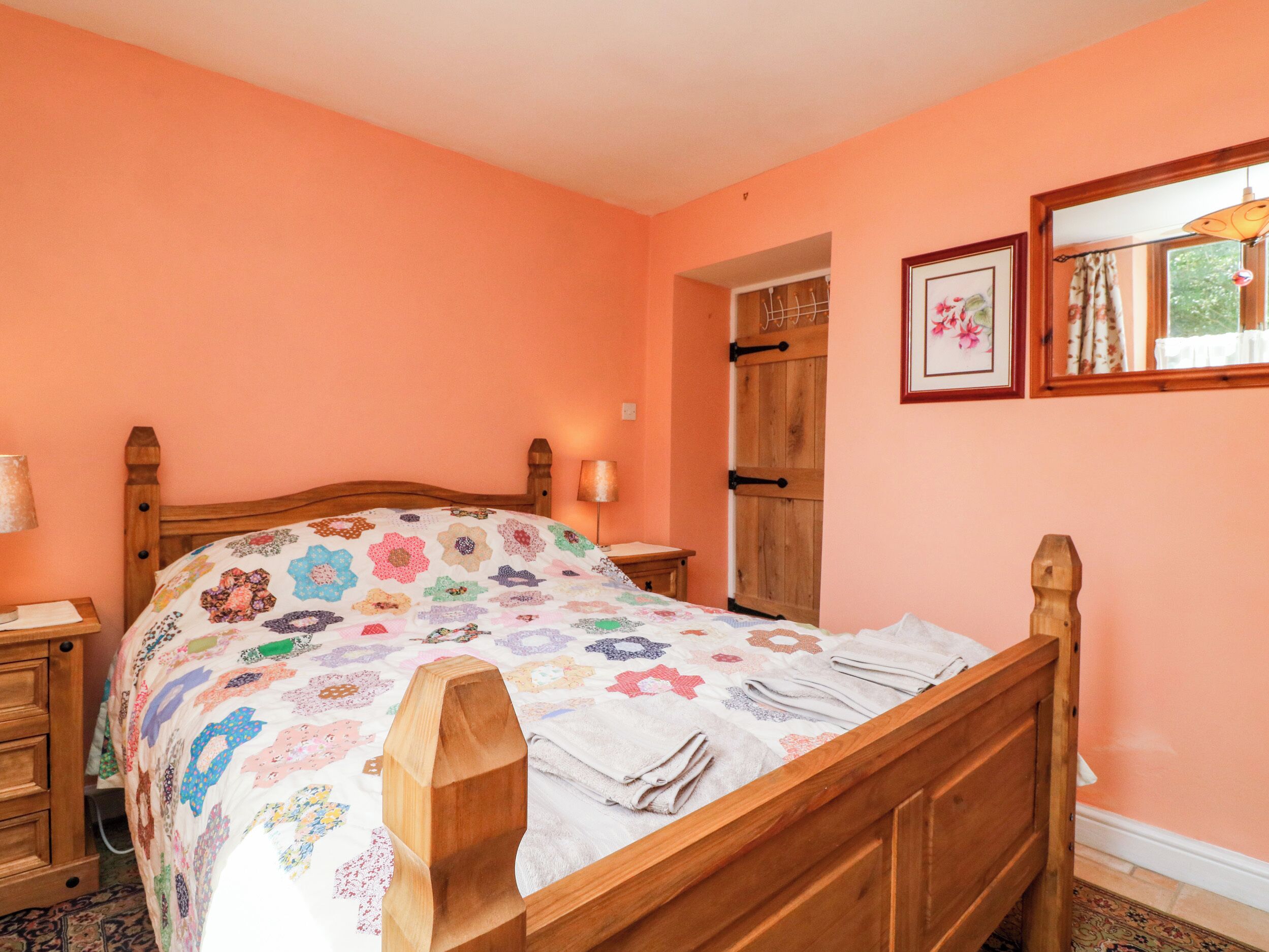 Een slaapkamer met een houten bed, een nachtkastje, een lamp, een deur en een lijst met een afbeelding aan de muur.