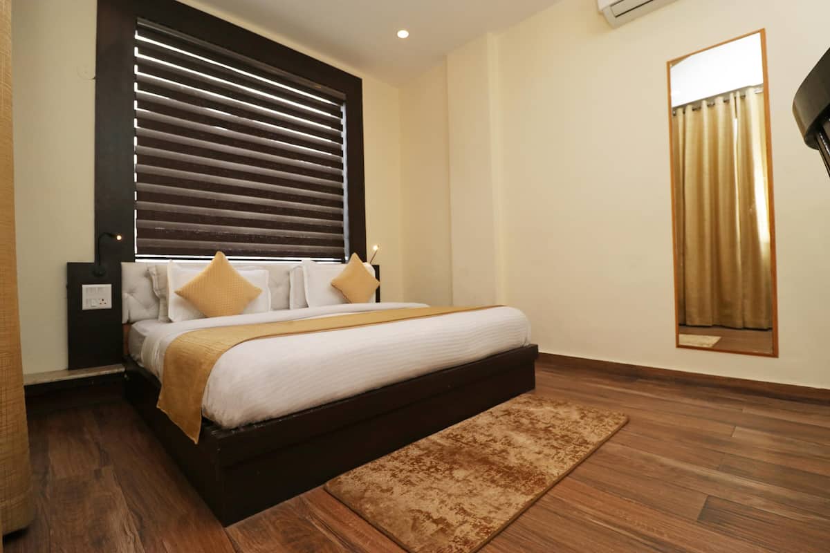 Un dormitorio con una cama grande, suelo de madera, cabecera con listones horizontales, mesita de noche y un espejo en la pared.