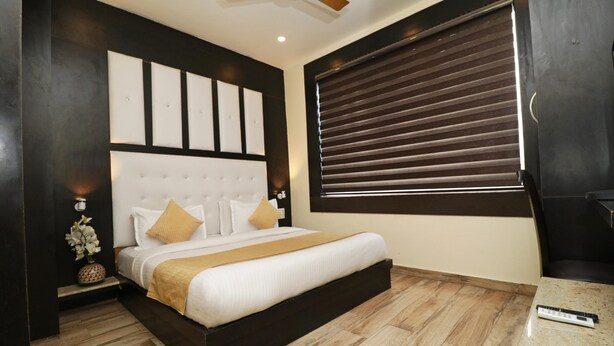 Un dormitorio moderno con una cama grande, un cabecero con decoración de pared, una mesita de noche con lámpara y una ventana con persianas.