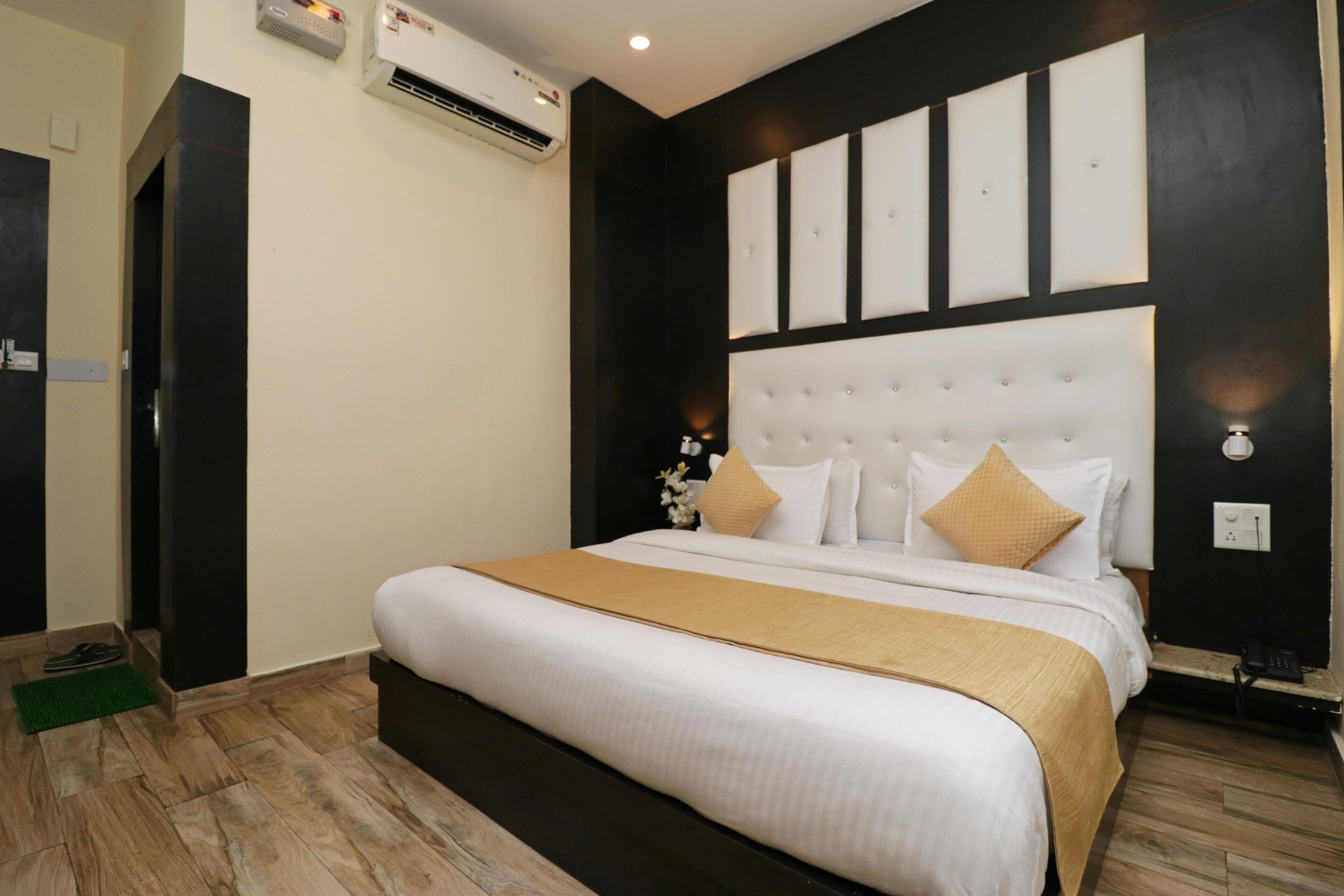 Habitación de hotel con una cama grande, cabecera con paneles, un tapete verde y un equipo de aire acondicionado.