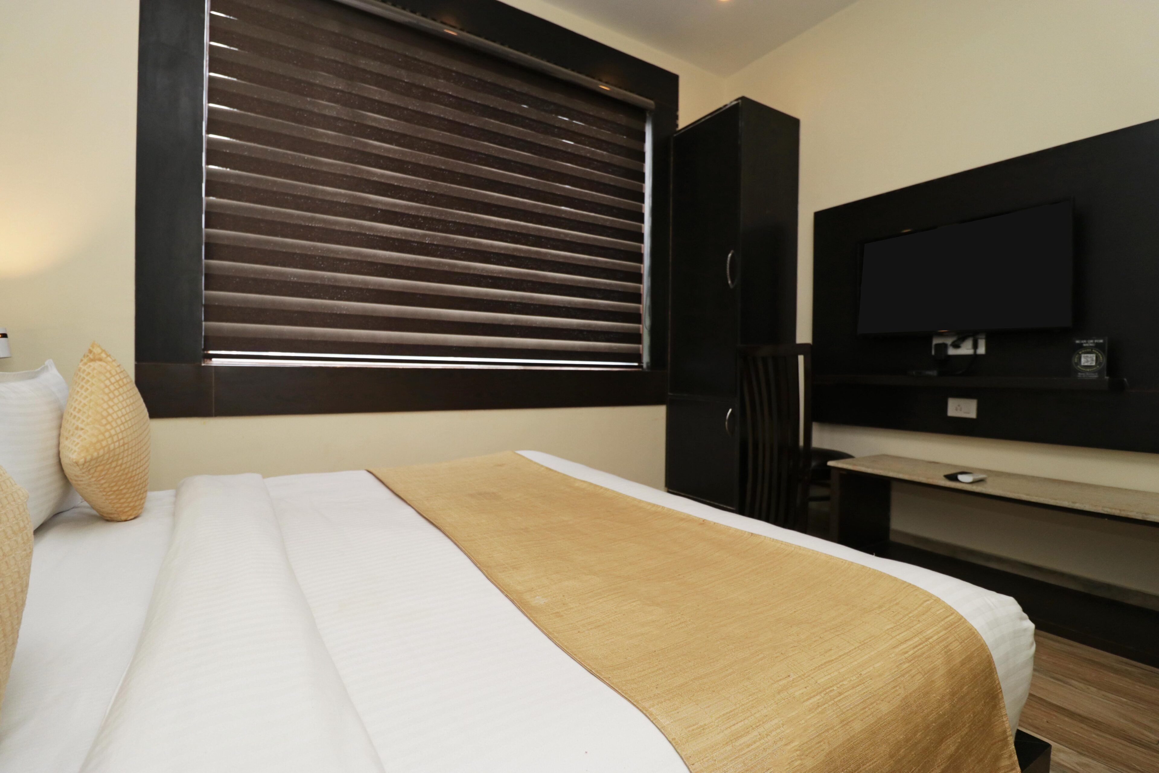 Una habitación de hotel con cama, televisión, escritorio y ventana con persianas.