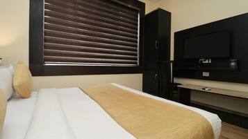 A hotel room with a bed, a television, a desk, and a window with blinds.