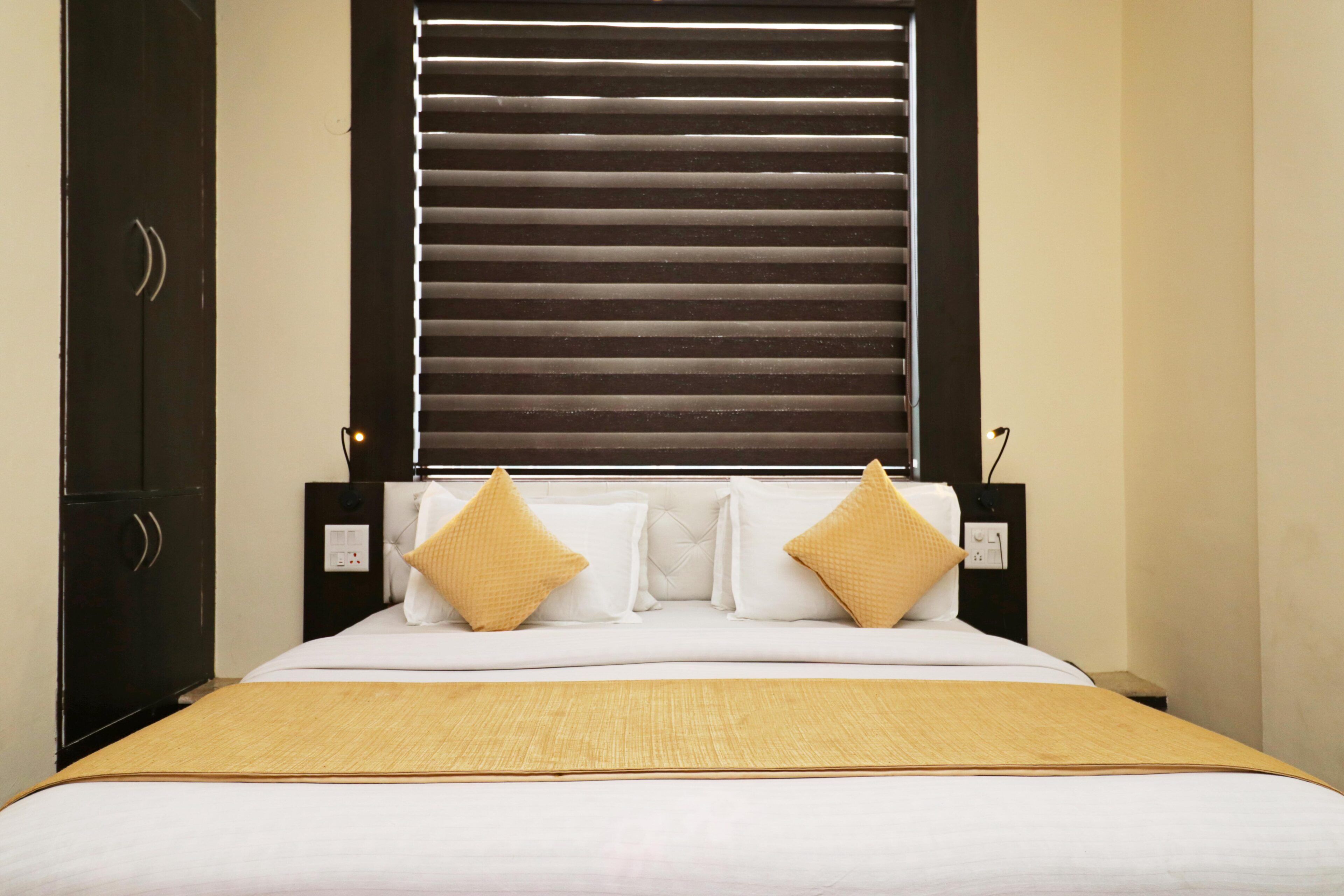 A hotel room with a bed, a nightstand, a wardrobe, and a window with blinds.