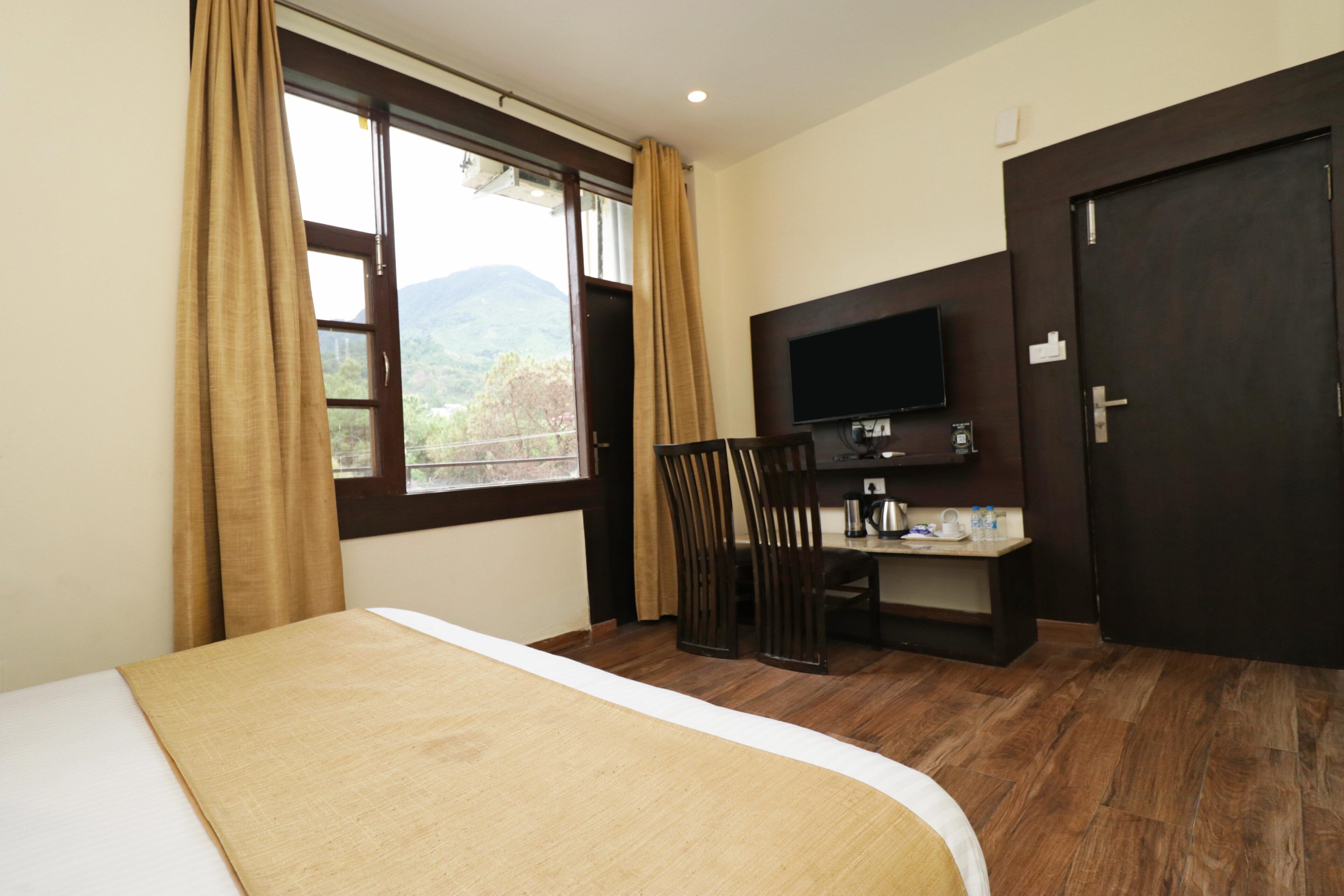 A hotel room with a bed, a TV mounted on the wall, a desk with a chair, and a view of the outdoors.