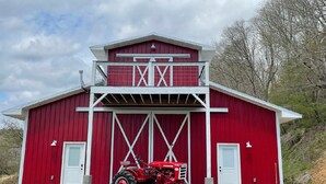 Une grange rouge avec une porte blanche et un tracteur rouge garé devant.