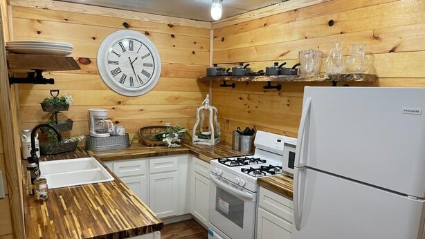 Une cuisine avec des murs en bois, un poêle blanc, un réfrigérateur et une horloge au mur.