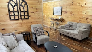 Un salon chaleureux avec un mur en bois, un canapé, un fauteuil, une table basse et une petite table accompagnée de tabourets.