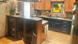 Une cuisine moderne avec des armoires en bois, un comptoir en granit, un îlot central intégré et une hotte de cuisinière en acier inoxydable.
