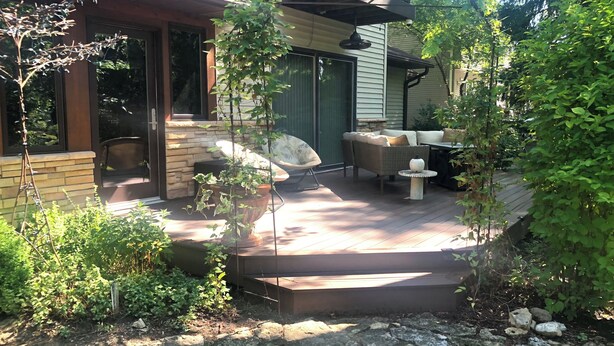 Une terrasse couverte avec des meubles d’extérieur, un chemin en pierre et une vue sur la maison.