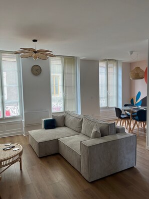 A modern living room with a sectional sofa, a dining table with chairs, and a ceiling fan.