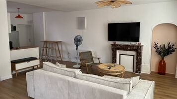 Ein Wohnzimmer mit einem großzügigen Ecksofa, einem Flachbildfernseher, einem Kamin und einem Essbereich mit einem Holztisch und Stühlen.
