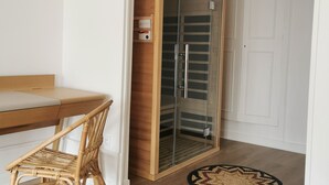 Une pièce comprenant une table à manger en bois, une chaise en osier, un dressing fermé par des parois de verre et un tapis à motifs sur le sol.