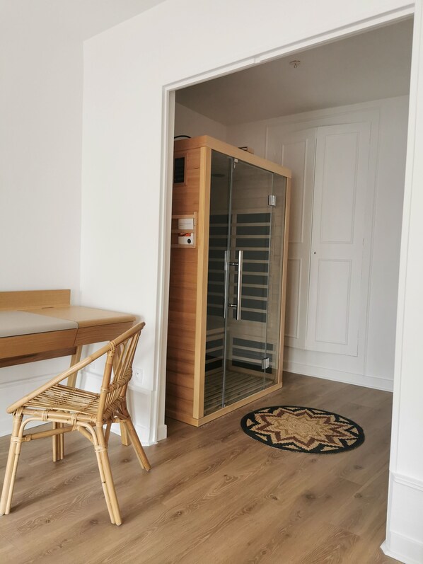 A room with a wooden dining table, a wicker chair, a glass-enclosed walk-in closet, and a patterned rug on the floor.