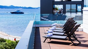 A modern rooftop terrace with sun loungers and a glass balustrade overlooking the sea.