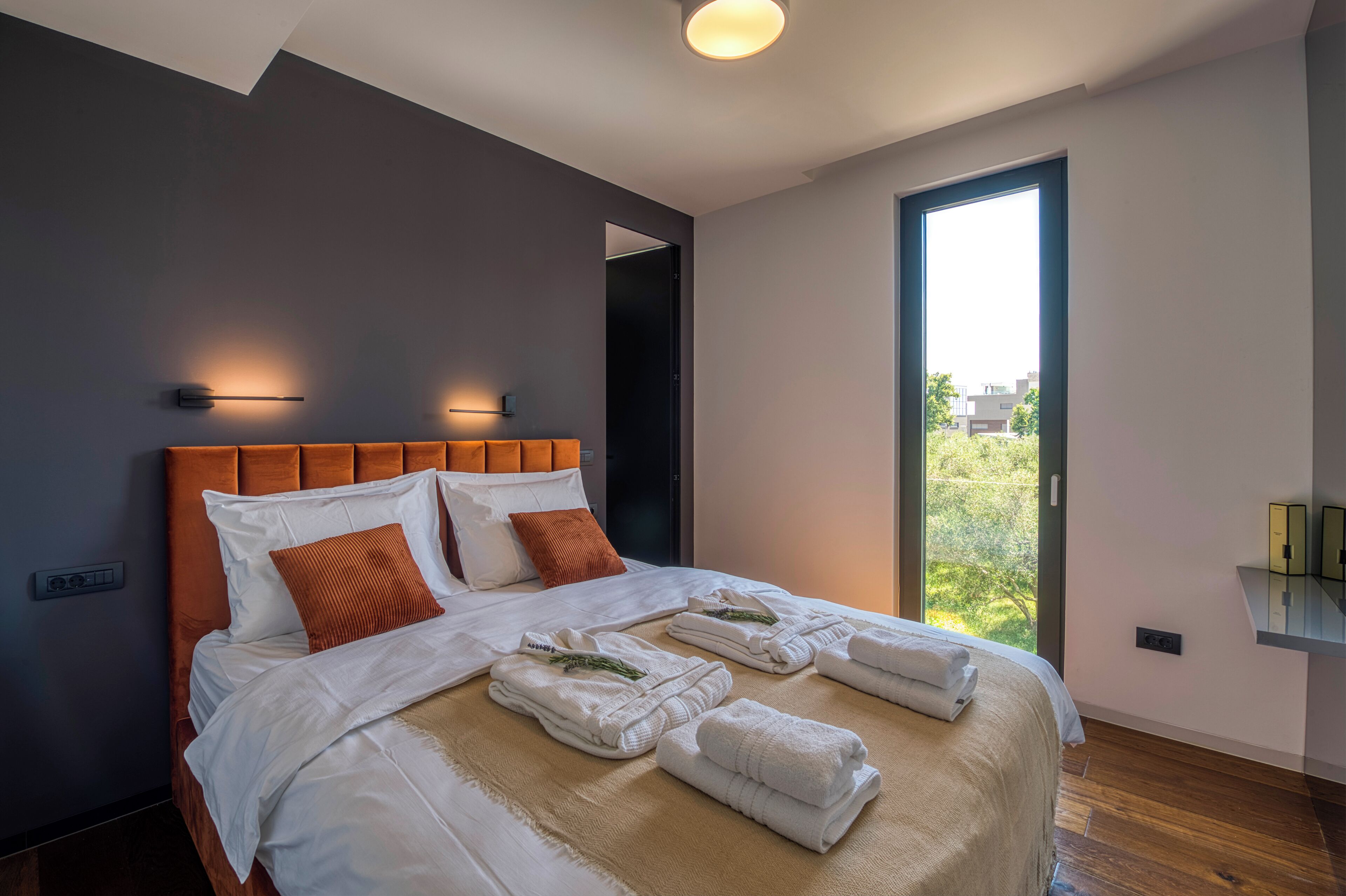 Ein modernes Hotelzimmer mit einem großen Bett, zwei Wandleuchten, Blick auf Grünfläche und einem kleinen Nachttisch.