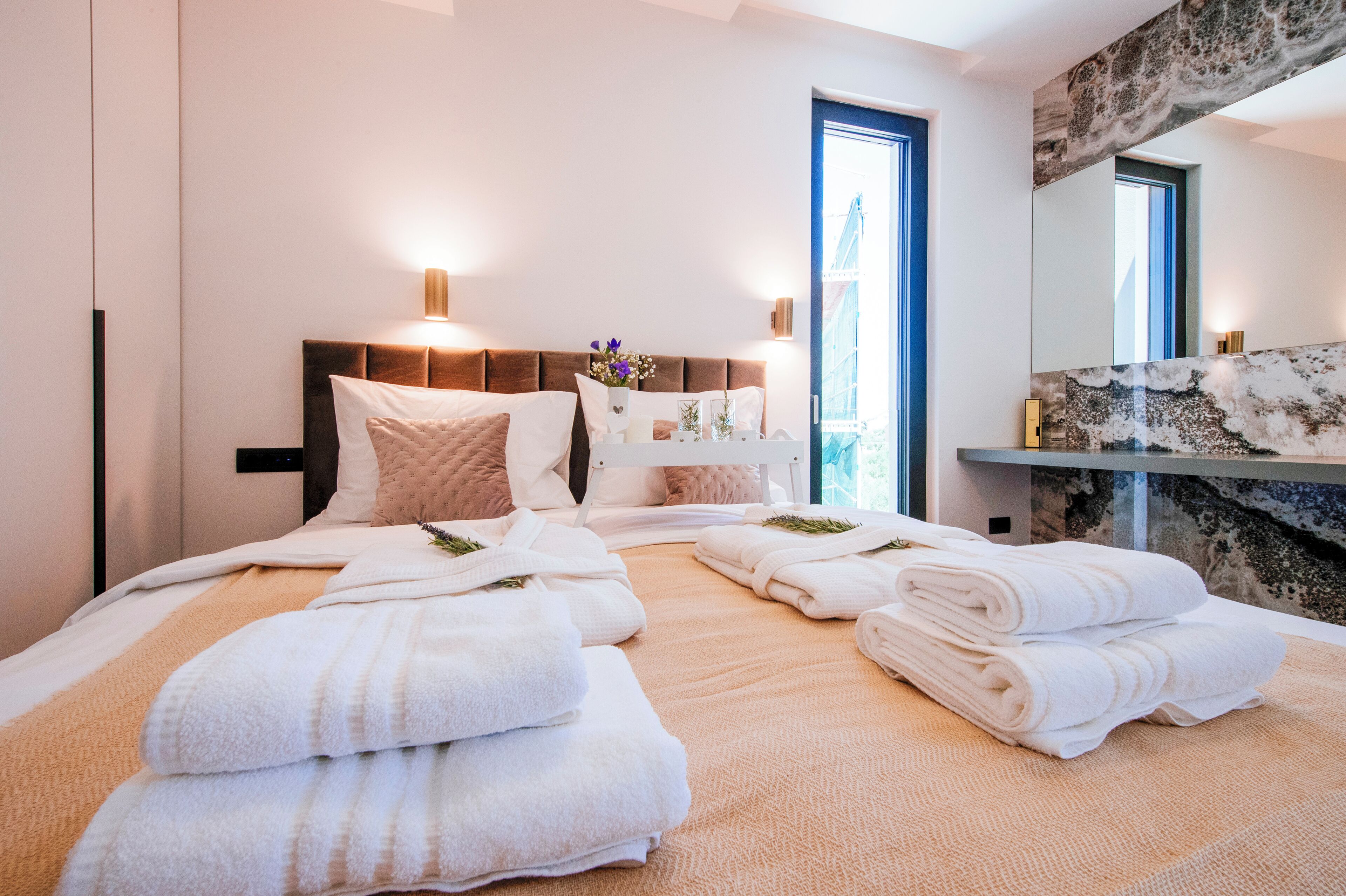 A hotel room with a bed, towels, a nightstand, a mirror, and a window.