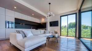 A modern living room with a sofa, a coffee table, and a view of the outdoors through large windows.