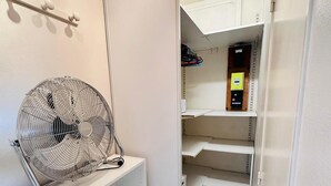 A hotel room with a white fan on a shelf, a wardrobe, and a glimpse of a bathroom with a toilet and a small shelf. - Appartement Ménilmontant (Paris)