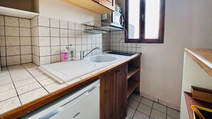 A compact kitchen with a dishwasher, wooden cabinets, a microwave, and a window providing natural light. - Appartement Ménilmontant (Paris)