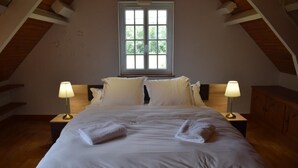 A neatly made bed in a room with a large window, two bedside lamps, and a wooden headboard. - Gîte 2/4 Personnes (Huisseau-sur-Mauves)