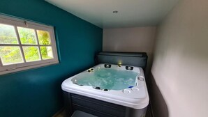 A small room with a hot tub, a window, and a bench. - Gîte 2/4 Personnes (Huisseau-sur-Mauves)