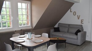 A modern living room with a dining area, a grey sofa, and a wall with the word "LOVE" written on it. - Gîte 2/4 Personnes (Huisseau-sur-Mauves)