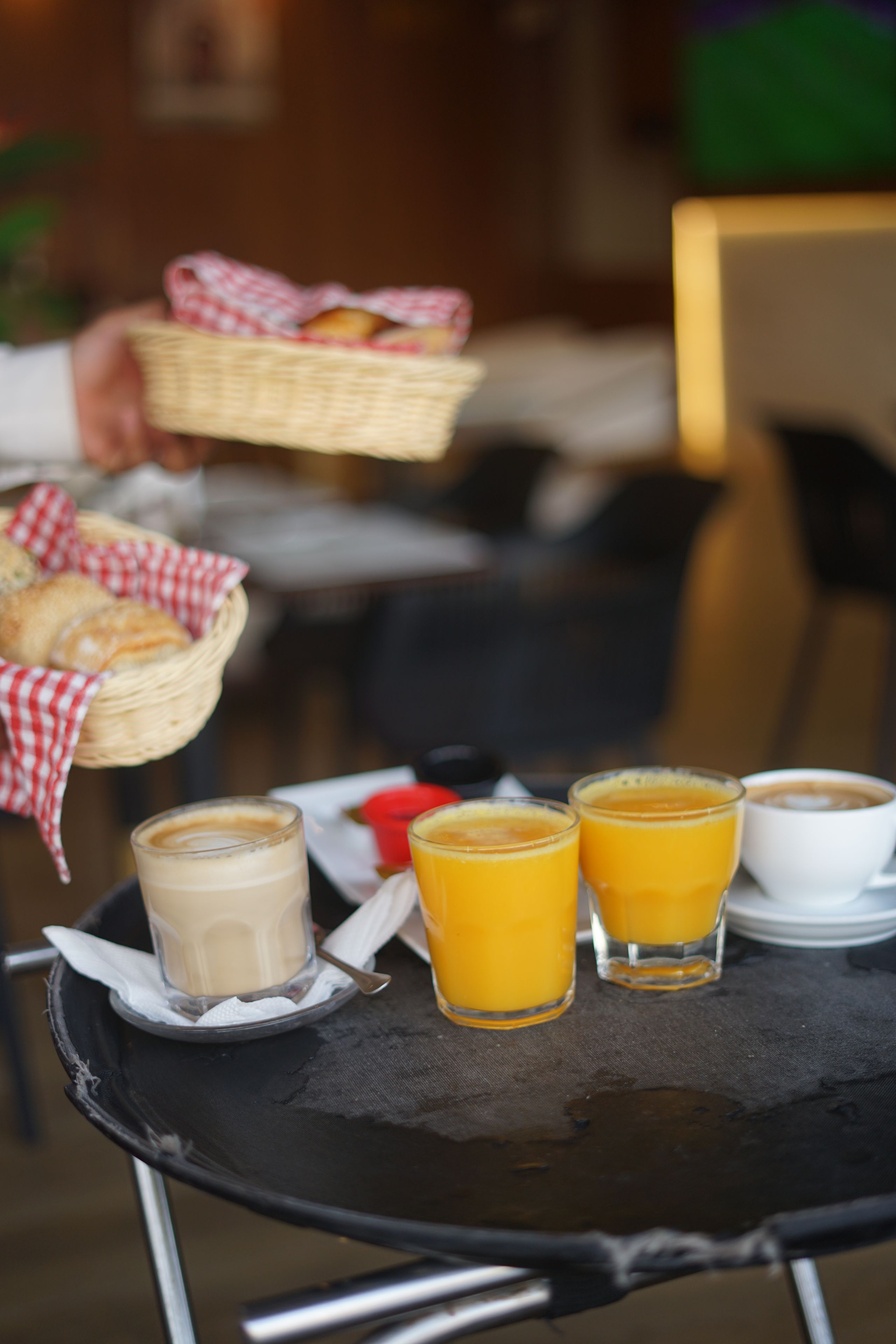 Een tafel met een broodmand, twee glaasjes sinaasappelsap en een kop koffie.
