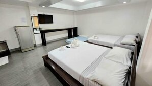A hotel room with two beds, a desk, a television, and a refrigerator. - MGG Casa Dela Playa (Boracay Island)