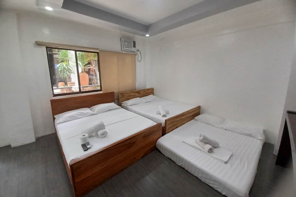 Habitación de hotel con dos camas individuales, cabecero de madera, ventana con vistas al exterior y un equipo de aire acondicionado en la pared.