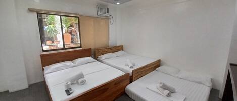 Habitación de hotel con dos camas individuales, cabecero de madera, ventana con vistas al exterior y un equipo de aire acondicionado en la pared.