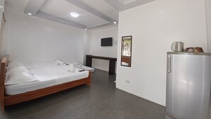 A hotel room with a bed, a desk, a TV, and a refrigerator. - MGG Casa Dela Playa (Boracay Island)