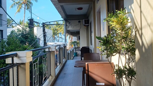 A balcony with a table and chairs, a potted plant, and a view of the street and palm trees. - MGG Casa Dela Playa (Boracay Island)