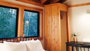 Una habitación de cabaña de madera con una cama, una mesa y una ventana con vistas a un bosque.
