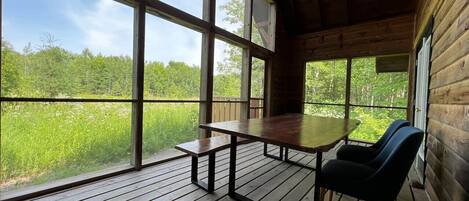 Un patio in legno con tavolo e panchina, ampie finestre che si affacciano su un paesaggio verde.