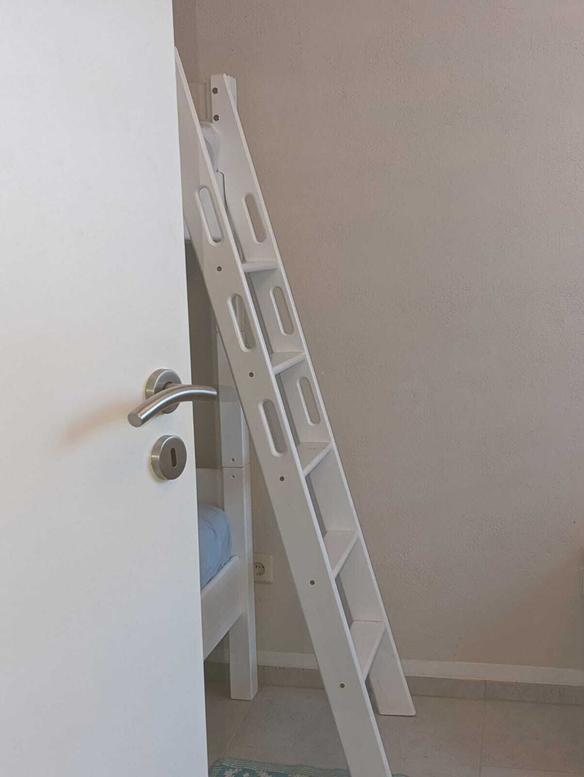 Una puerta blanca con un picaporte metálico y una escalera de mano apoyada en la pared.