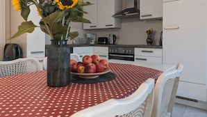 A kitchen with white cabinets, a stove, and a sink. There is a table with a red polka dot tablecloth and a vase with sunflowers. - Double vacation bungalow in the middle of the Schorfheide (Joachimsthal)