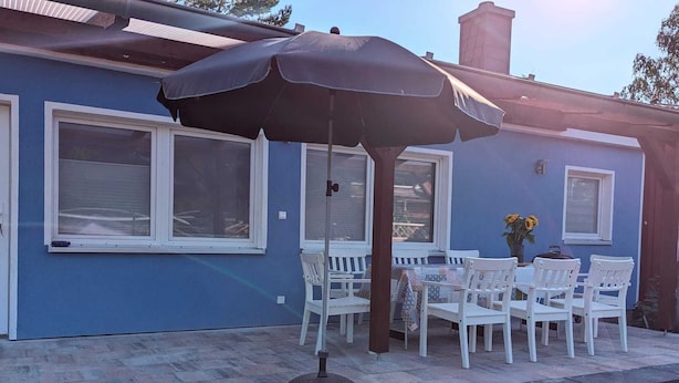 An outdoor patio with a table and chairs, a large umbrella, and a flower vase. - Double vacation bungalow in the middle of the Schorfheide (Joachimsthal)